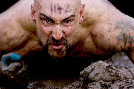 A closeup shot of a bare chested man with a race number written on his forehead crawling through deep mud as part of the annual Tough Guy obstacle race.
