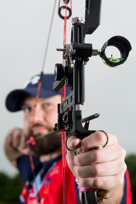 Head on shot of a sport archer pulling back on his high-tech recurve bow with the arrow tip in sharp focus and the depth of field falling away to the archer's face. 