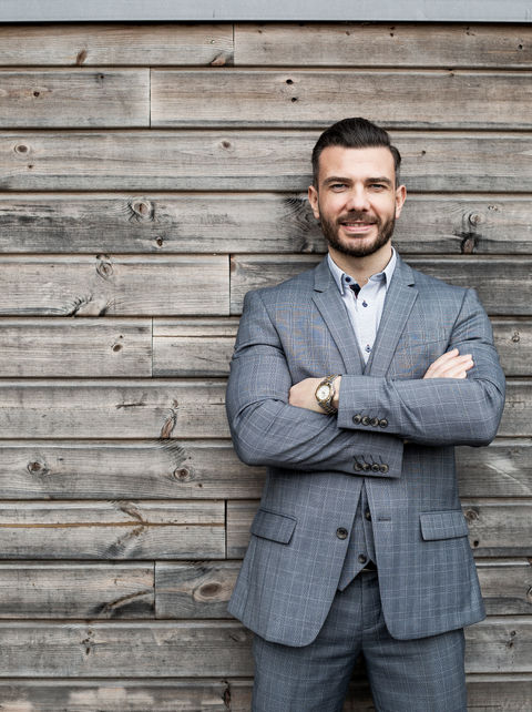 Business portrait photography of a man in a smart suit leaning arms  folding on an external wooden panel.