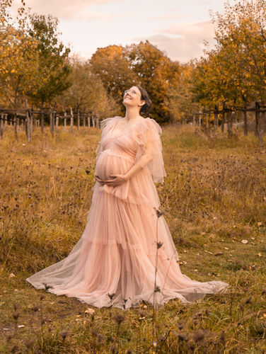 schwangere beim Babybauchshooting mit rosa Tüllkleid auf einer Obstbaumwiese