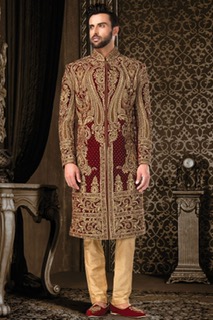 A groom wearing a luxurious gold and maroon sherwani with intricate embroidery, standing in an opulent setting with traditional Indian wedding decor.