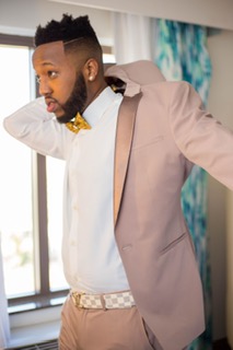 A groom putting on a blush-colored suit jacket, pairing it with a white dress shirt and a mustard-yellow bow tie, creating a unique and stylish wedding ensemble.