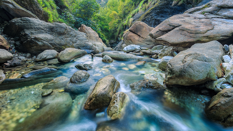 Clear water stream flows over smooth rocks between lush green, rocky banks.