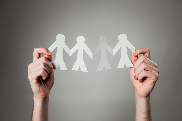 Two hands holding a chain of paper cut-out figures against a grey background
