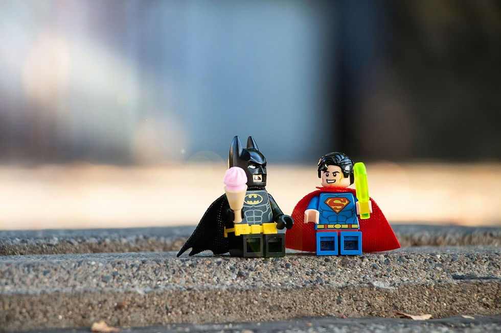 Two Lego minifigures of Batman and Superman standing side by side on a concrete surface