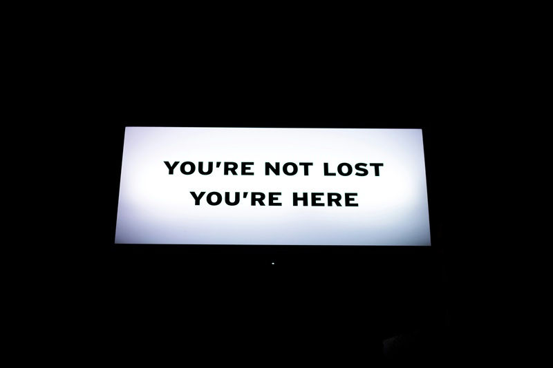 Bold sign reading "You're Not Lost, You're Here" — a reminder for early-stage founders that uncertainty is part of the startup validation journey