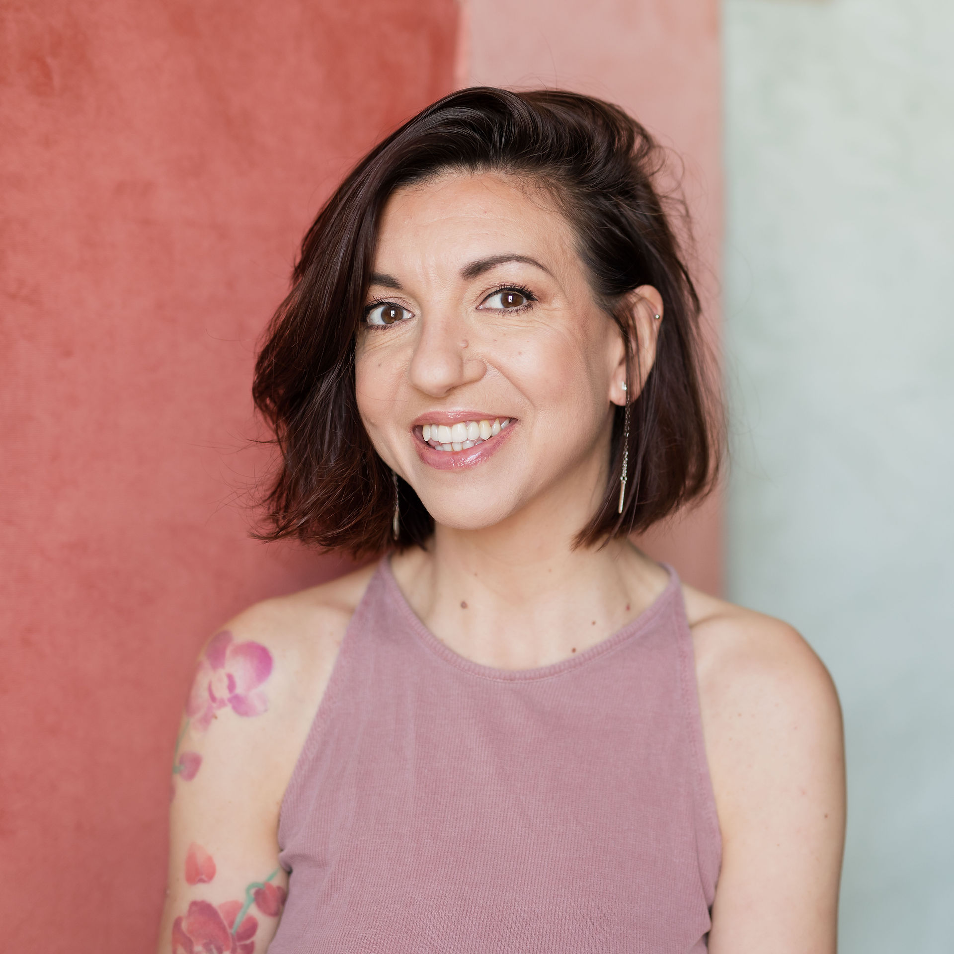 Femme souriante tatouée devant un fond rose