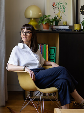 Portrait professionnel d'une femme à lunettes assise sur une chaise design jaune dans un intérieur moderne.