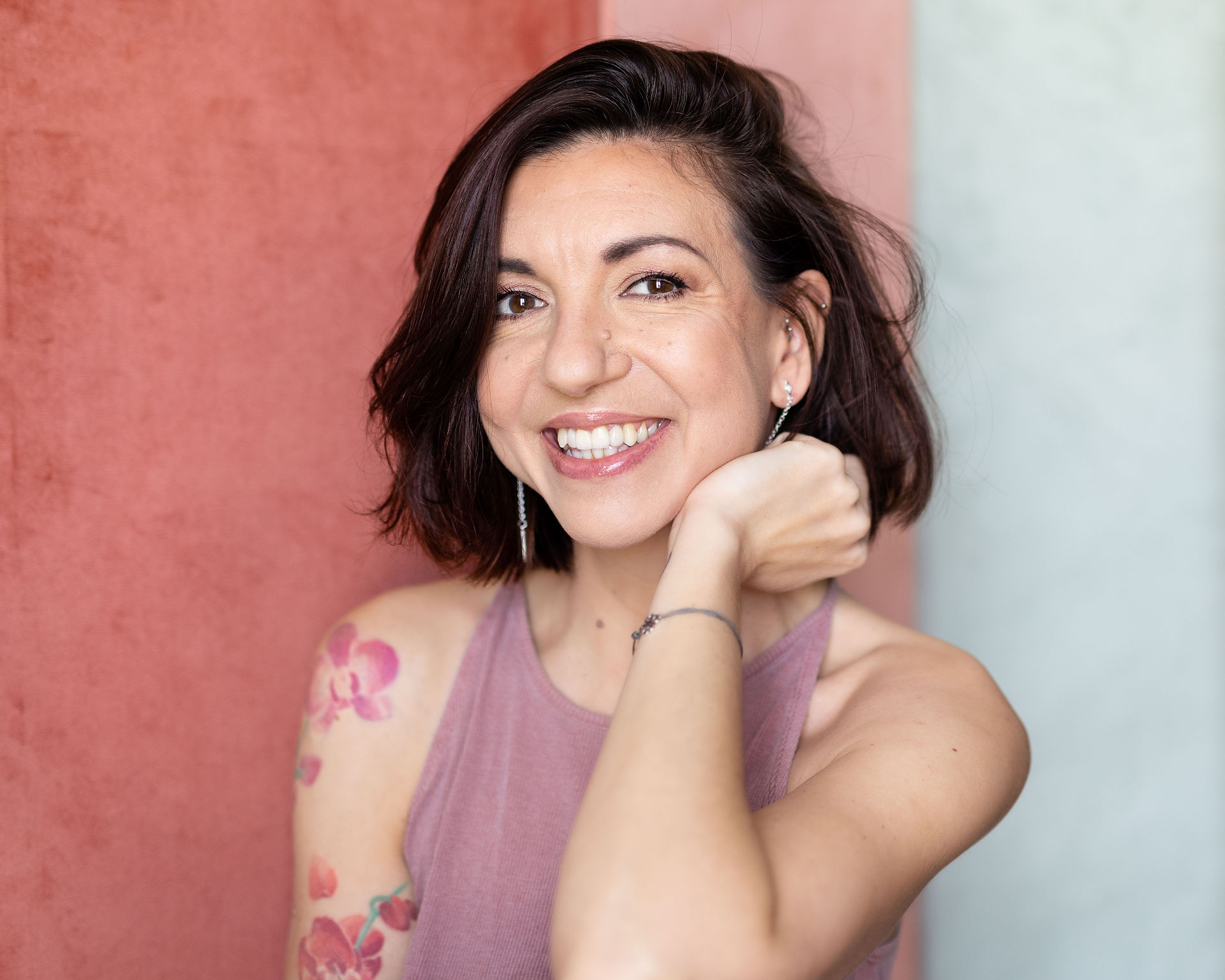 Femme souriante tatouée devant un fond rose