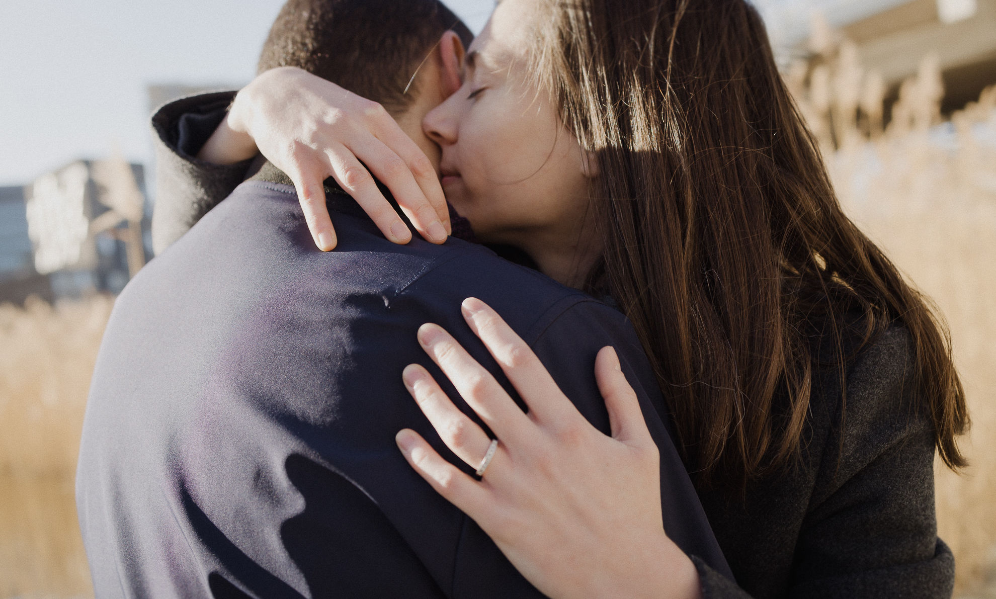 Gros plan d'un couple qui s'enlace tendrement avec une alliance visible à la main de la femme.