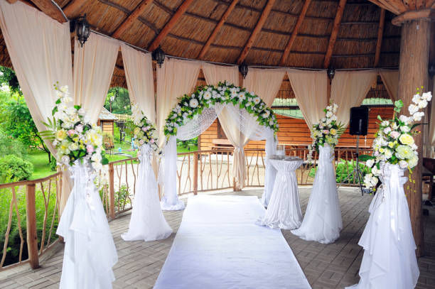 Elegant outdoor wedding setup under gazebo with floral arch and white drapery.