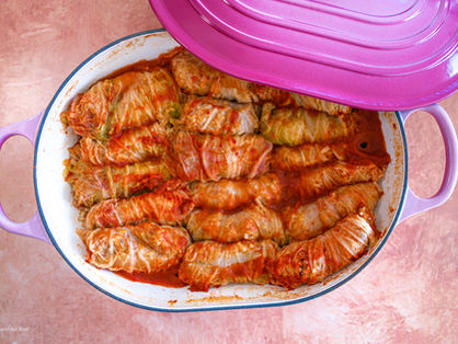 a pink large shallow pot with an enamel beige interior with lots of stuffed cabbage rolls and lots of tomato paste