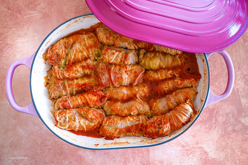 a pink large shallow pot with an enamel beige interior with lots of stuffed cabbage rolls and lots of tomato paste