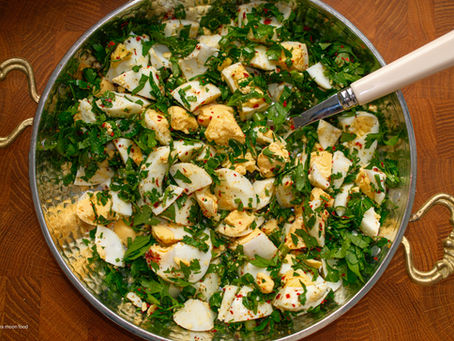 Metal bowl of chopped hard-boiled eggs, parsley, and red pepper flakes with a spoon on a wooden table