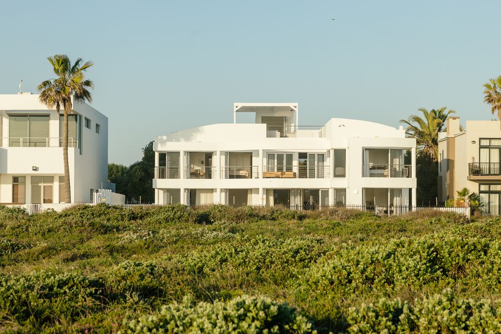 Modern white beach villa behind coastal greenery