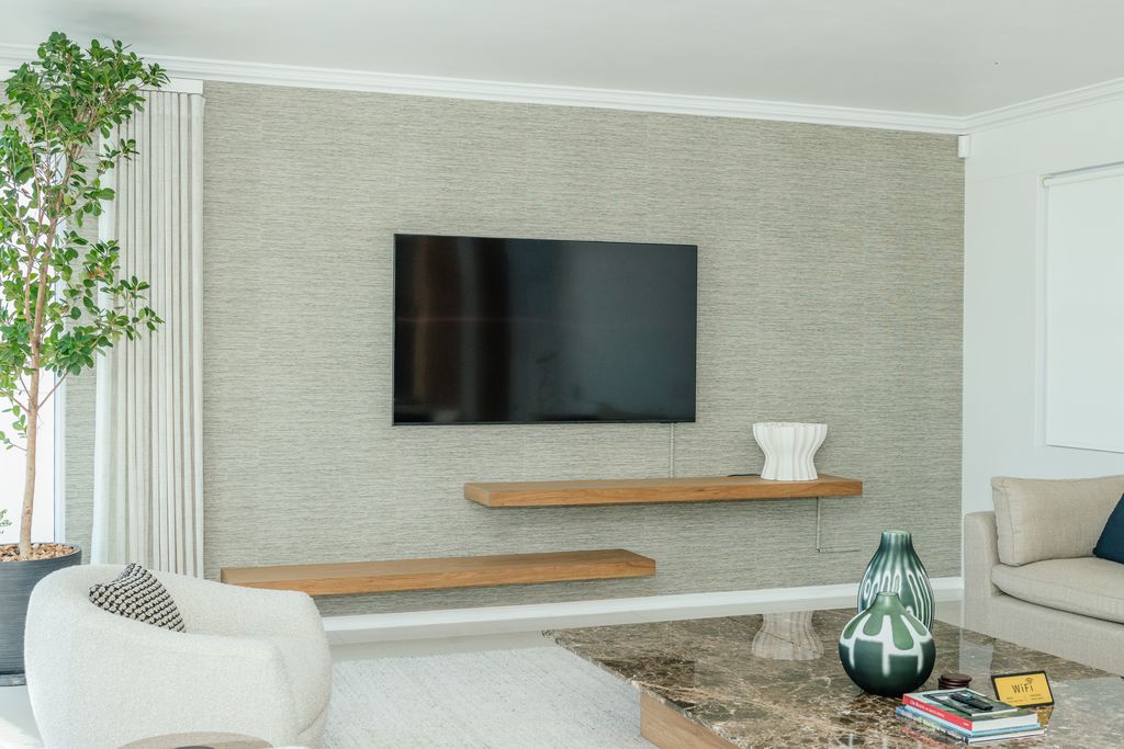 Wall-mounted TV above floating wooden shelves in a living room.