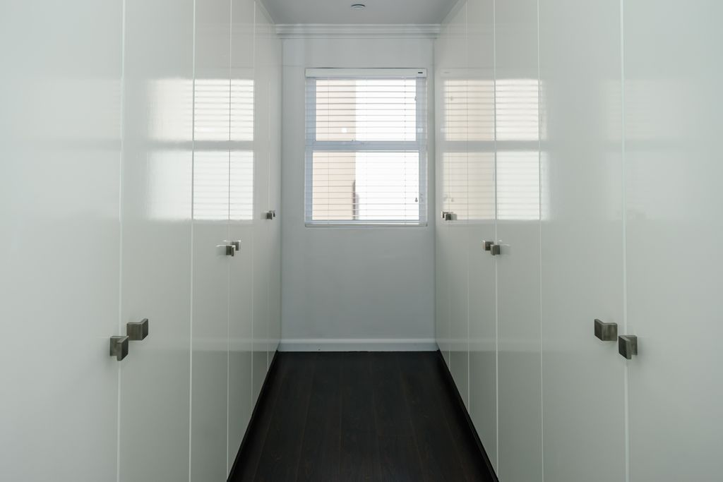 Modern white walk-in closet with glossy doors and window.