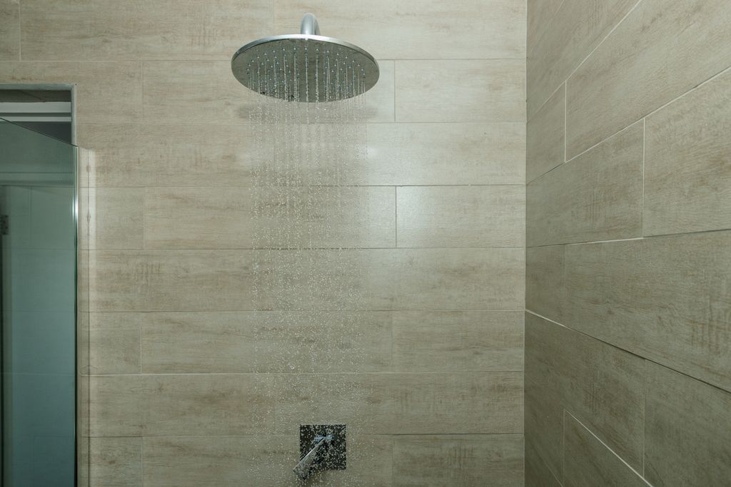 Rainfall shower head running in a tiled bathroom.