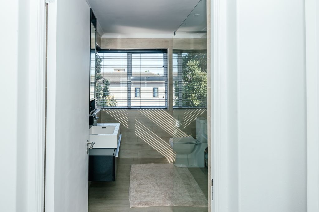Modern bathroom with white sink, toilet, and window blinds.