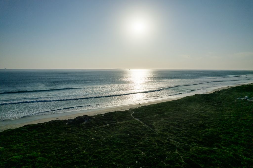 Aerial view of a sunny beach with waves and green hills.