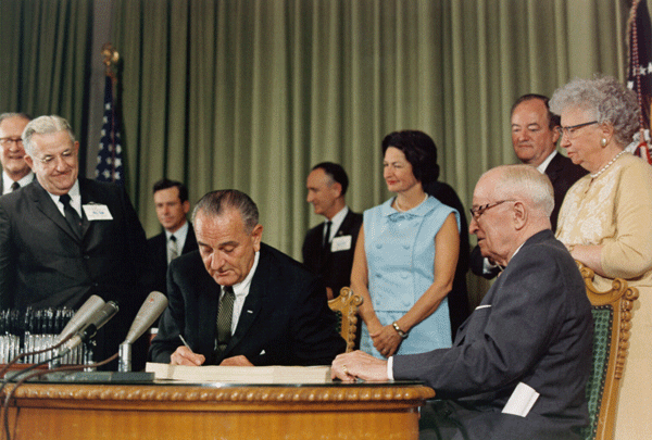 Democratic Pres. Lyndon Johnson signing Medicare into law with Pres. Truman, also a Democrat, looking on.