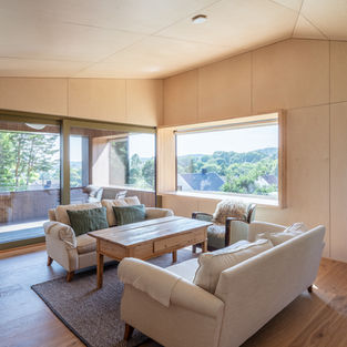 Attic living room with timber lining, sloped ceiling, picture window and balcony.