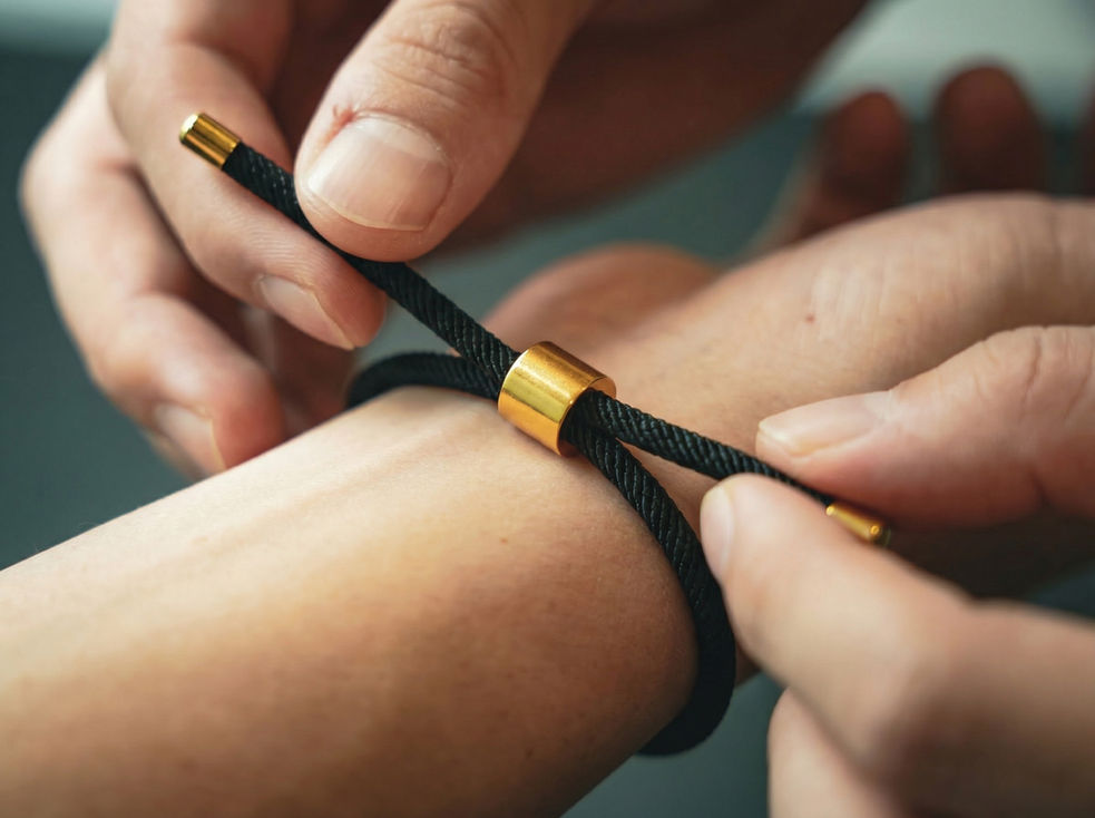 Mains ajustant un bracelet noir aux accents dorés