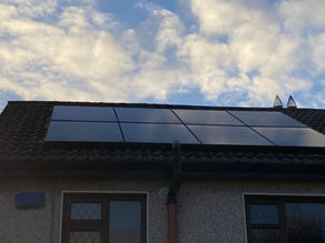 Solar panels on a tiled roof under a partly cloudy sky. The house has beige walls and dark-framed windows, creating a tranquil setting.