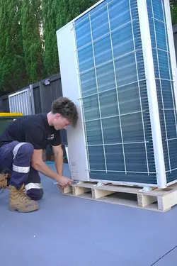 A Dream Air Conditioning technician uses a wrench to install a large outdoor compressor unit on a wo