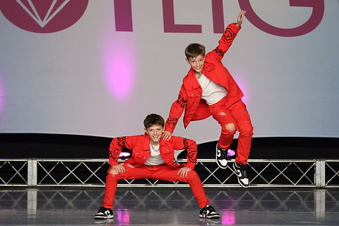 Two boys in red dance outfits performing a dynamic leap and pose on stage
