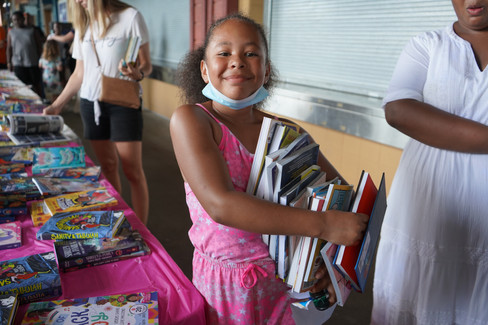 A child smiles with a precarious stack of 10-15 new books from the Summer Block Party.