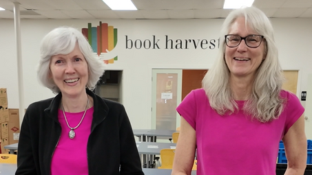 Volunteers Sharon and Linda smile at the camera in the Book Harvest book processing area during their interview.