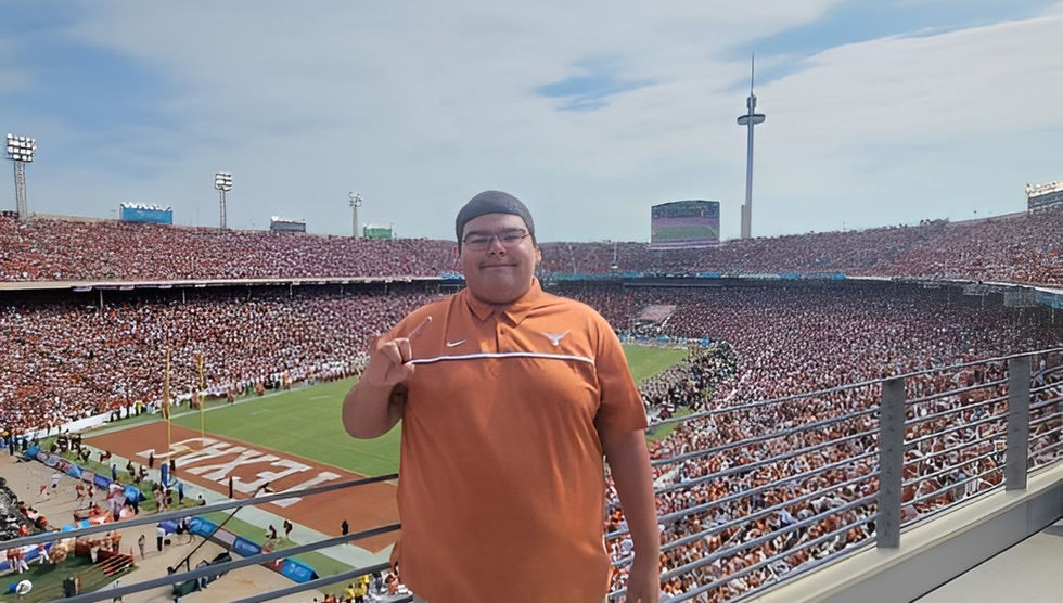Michael Trevino Jr at his seats at the Texas vs Oklahoma Football Game throwing up the Hook'em hand sign. 