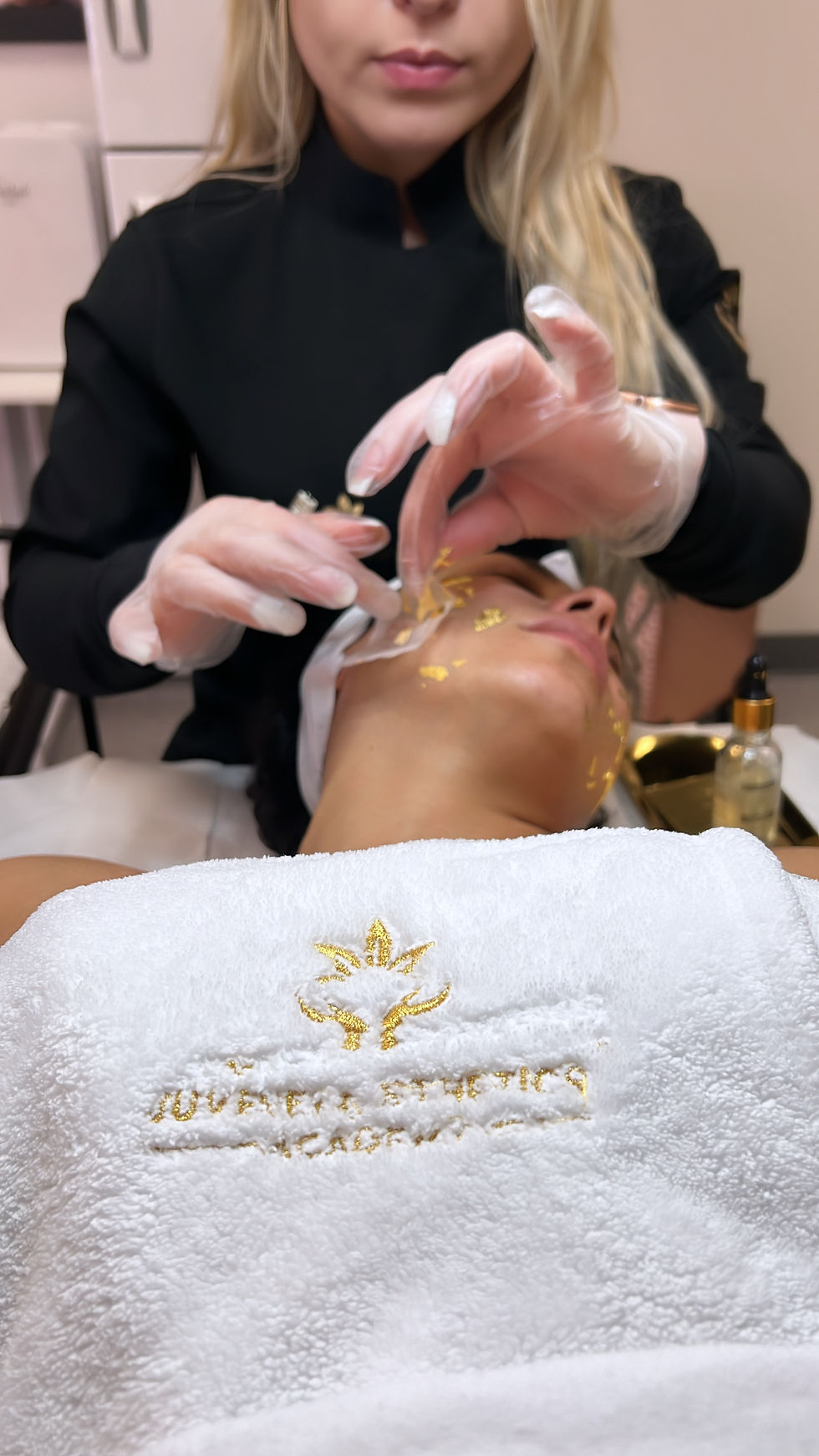 Juvenex 24K gold facial application — student applying gold-infused mask or serum under instructor supervision.