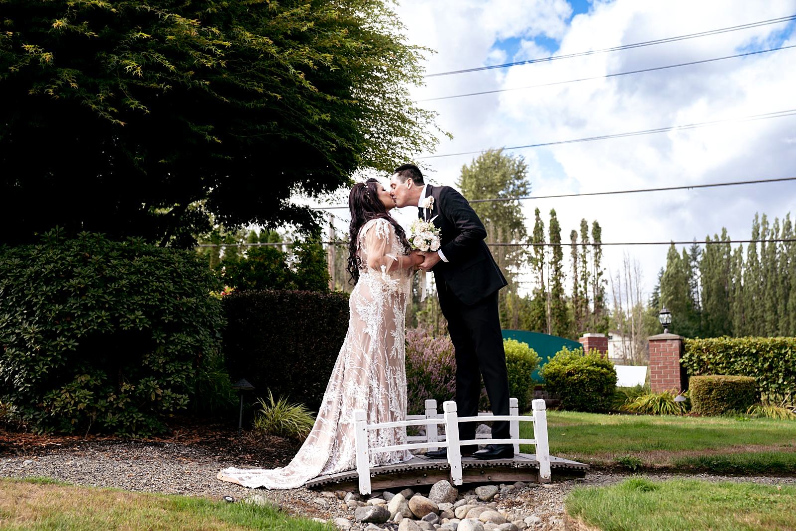 Newlyweds kissing on the lawn beside the little white bridge