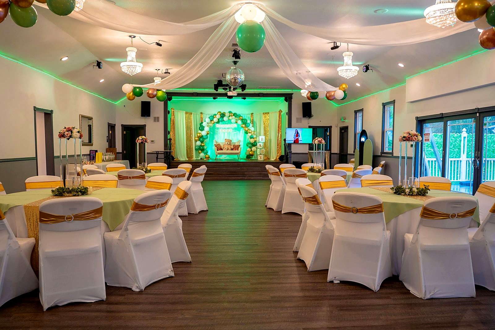 Main hall set for a shower – crystal chandeliers, draped ceiling and a balloon-arch stage