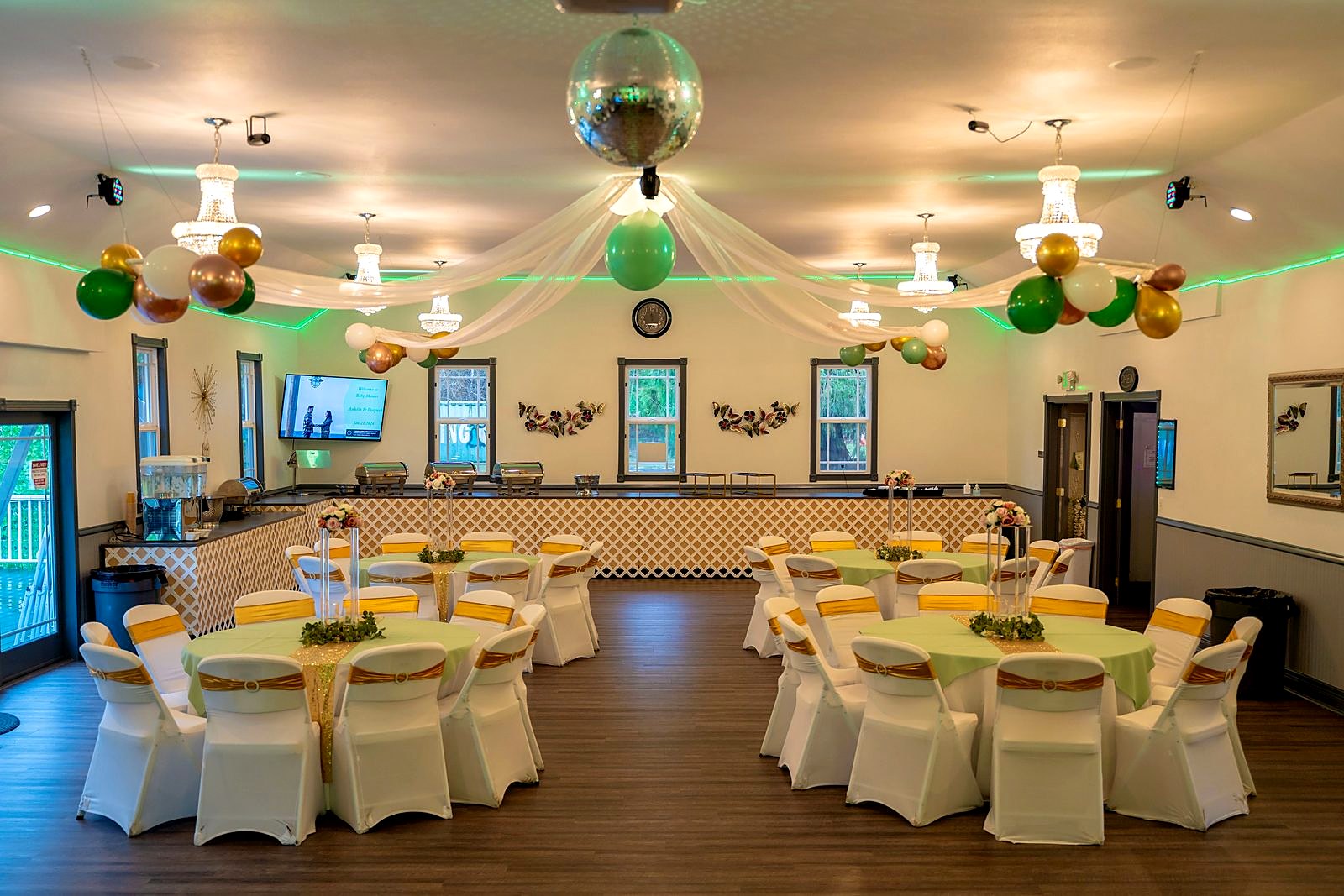Main hall with round tables, gold chair sashes, disco ball and the buffet counter