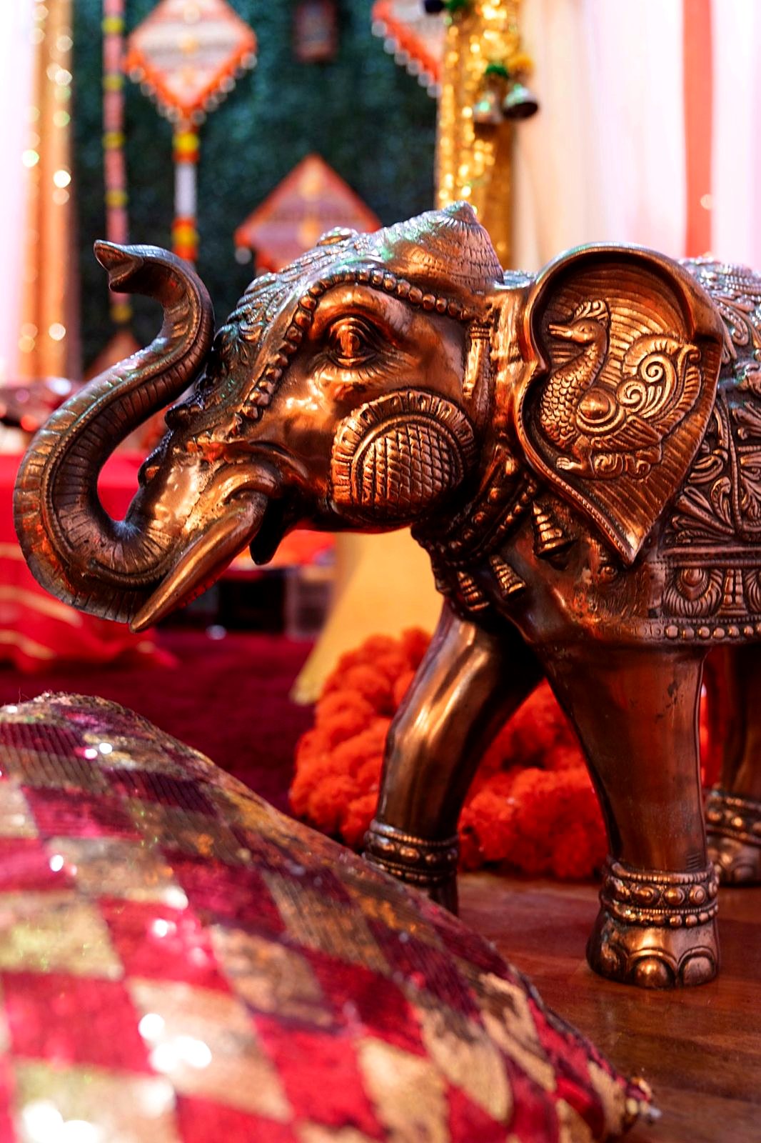 Brass elephant beside the mandap with marigolds and a sequin cushion