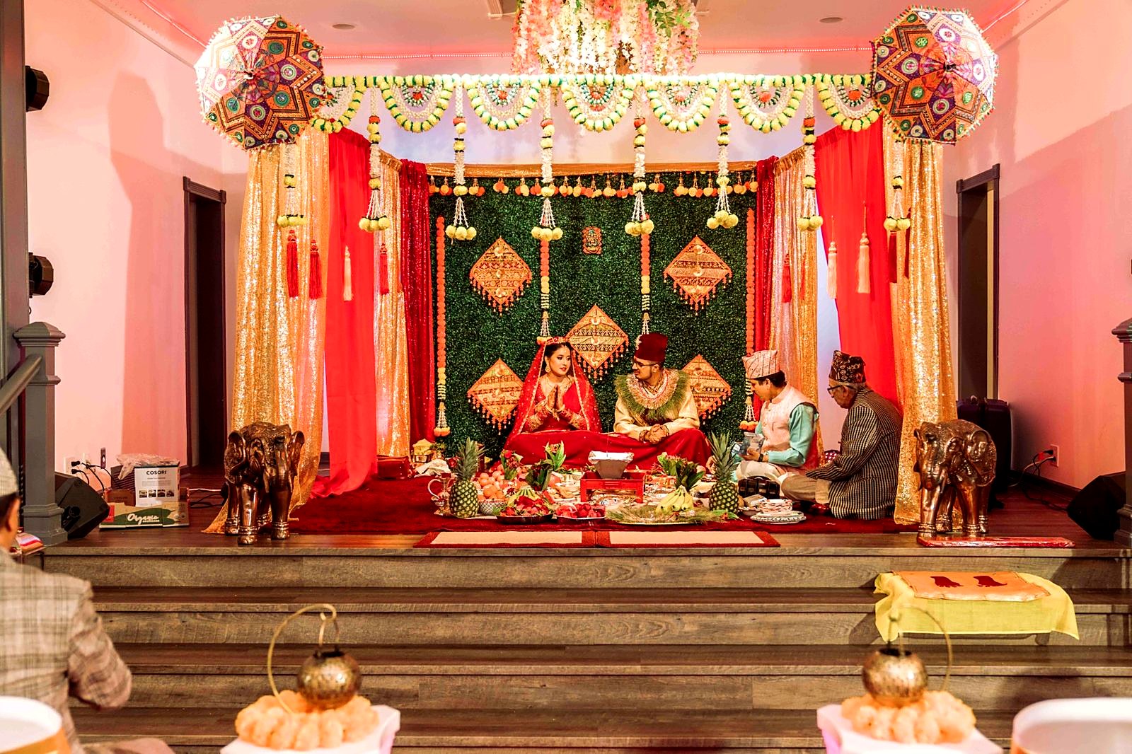 Wedding ceremony on the main stage – red and gold mandap with embroidered umbrellas, marigold strands and brass elephants