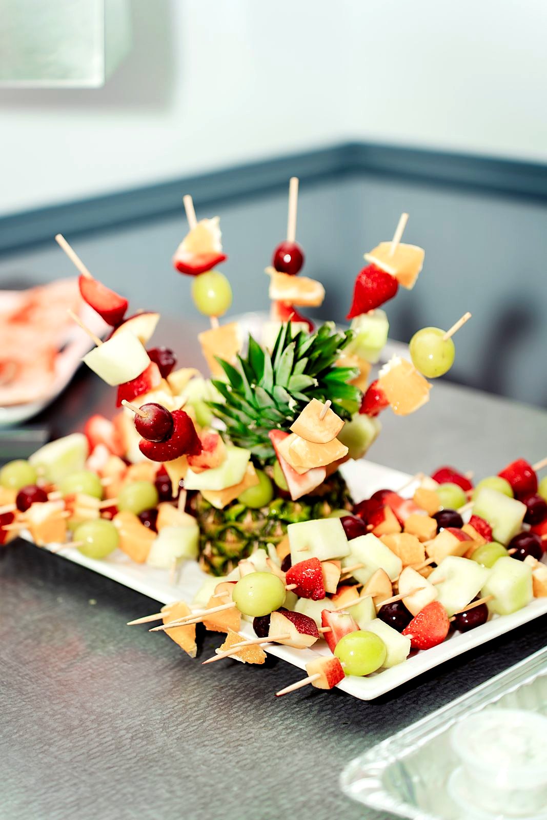 Fruit skewer display around a pineapple centerpiece – grapes, strawberries, melon and orange