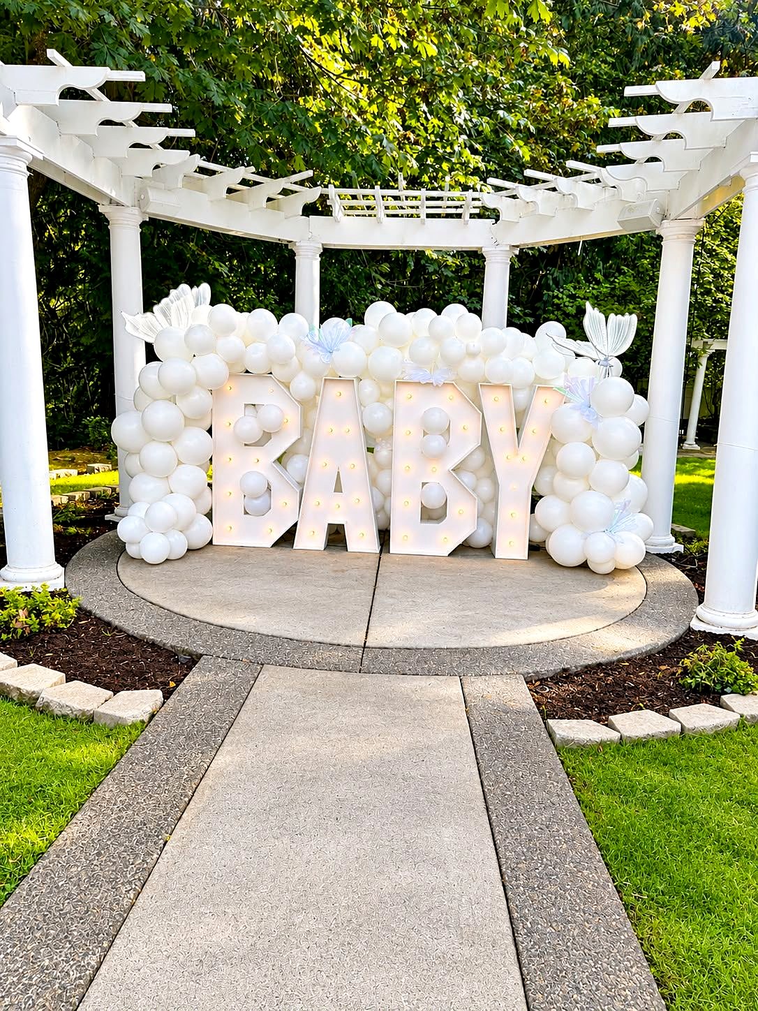 Light-up BABY marquee letters in a wall of white balloons under the garden pergola