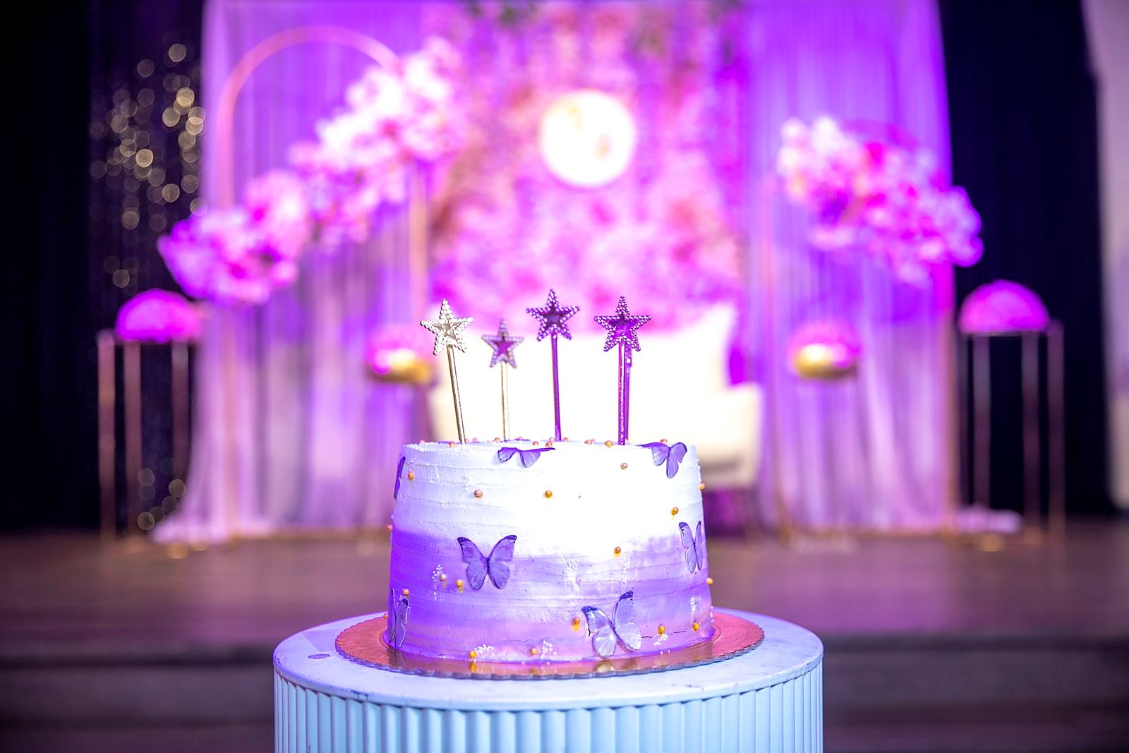 Lavender ombré butterfly cake with star toppers in front of a floral moon-arch stage