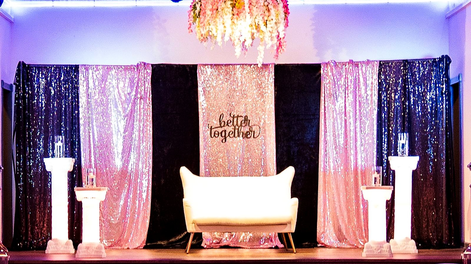 Stage with black and pink sequin drapes, white columns, a loveseat and a hanging wisteria chandelier under a "better together" sign