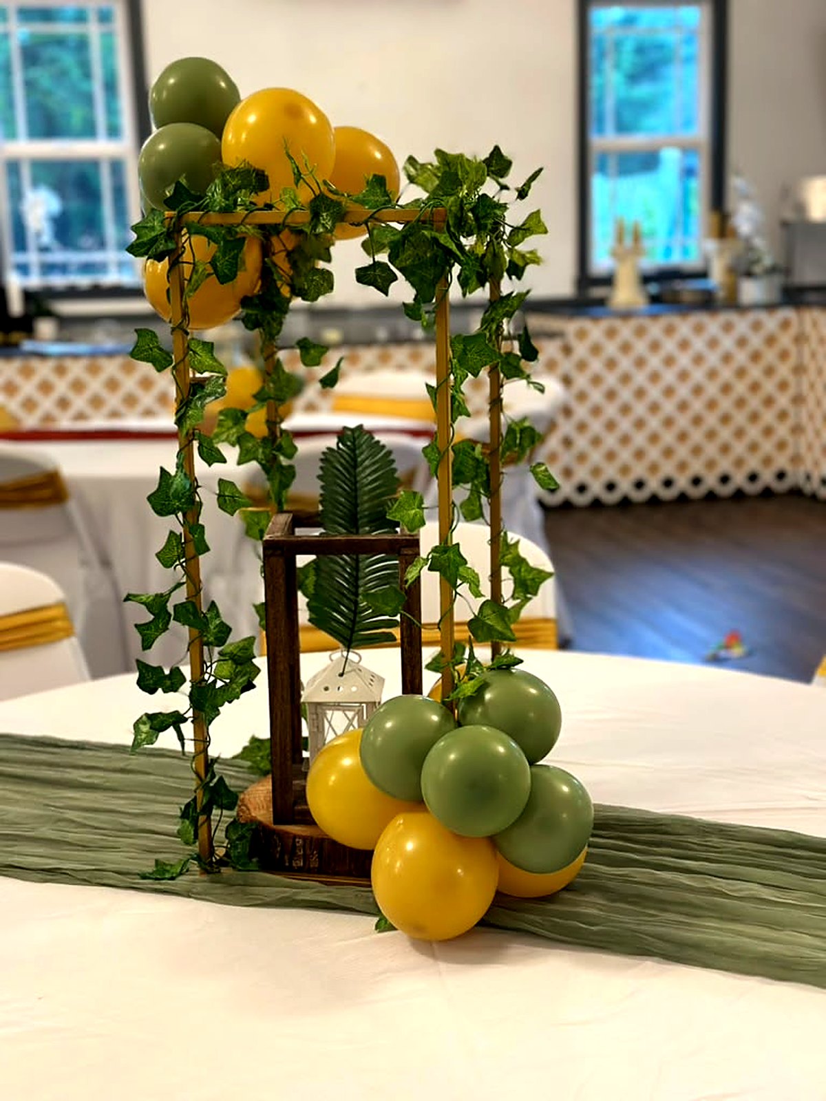 Jungle-theme table centerpiece – gold frame with ivy, wooden lantern and sage and mustard balloons