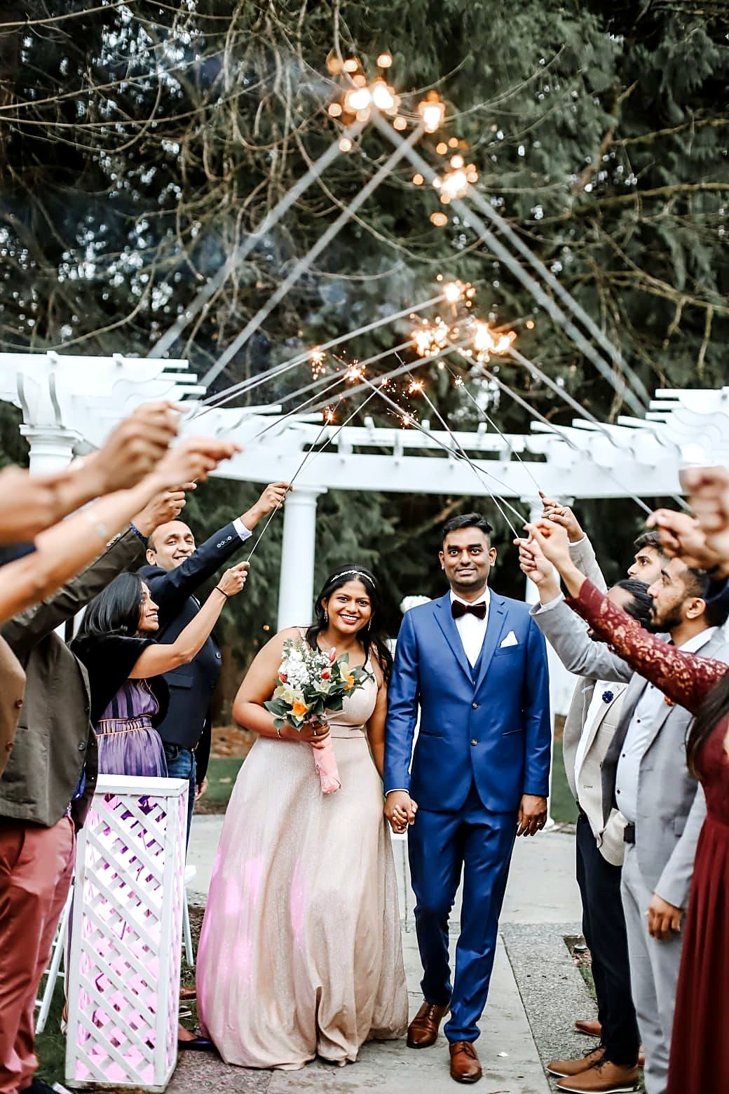 Newlyweds walking through a sparkler send-off by the garden pergola