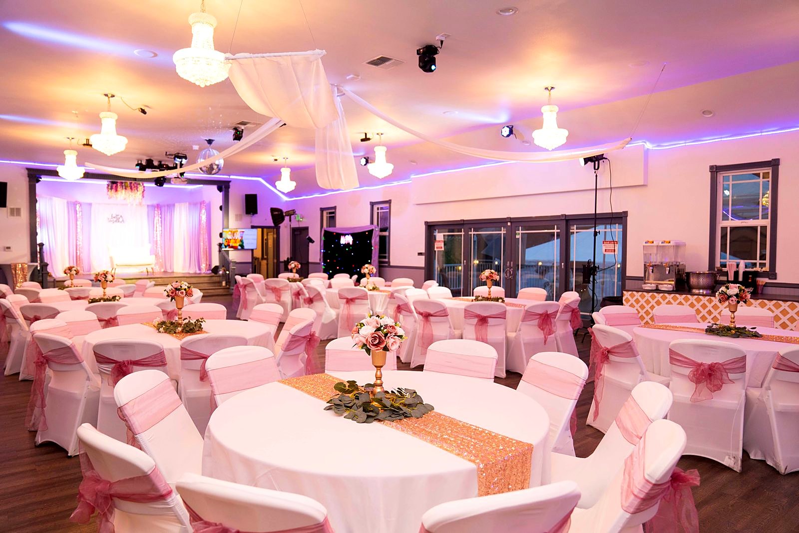 Main hall set for a reception – crystal chandeliers, draped ceiling, blush chair sashes and rose centerpieces