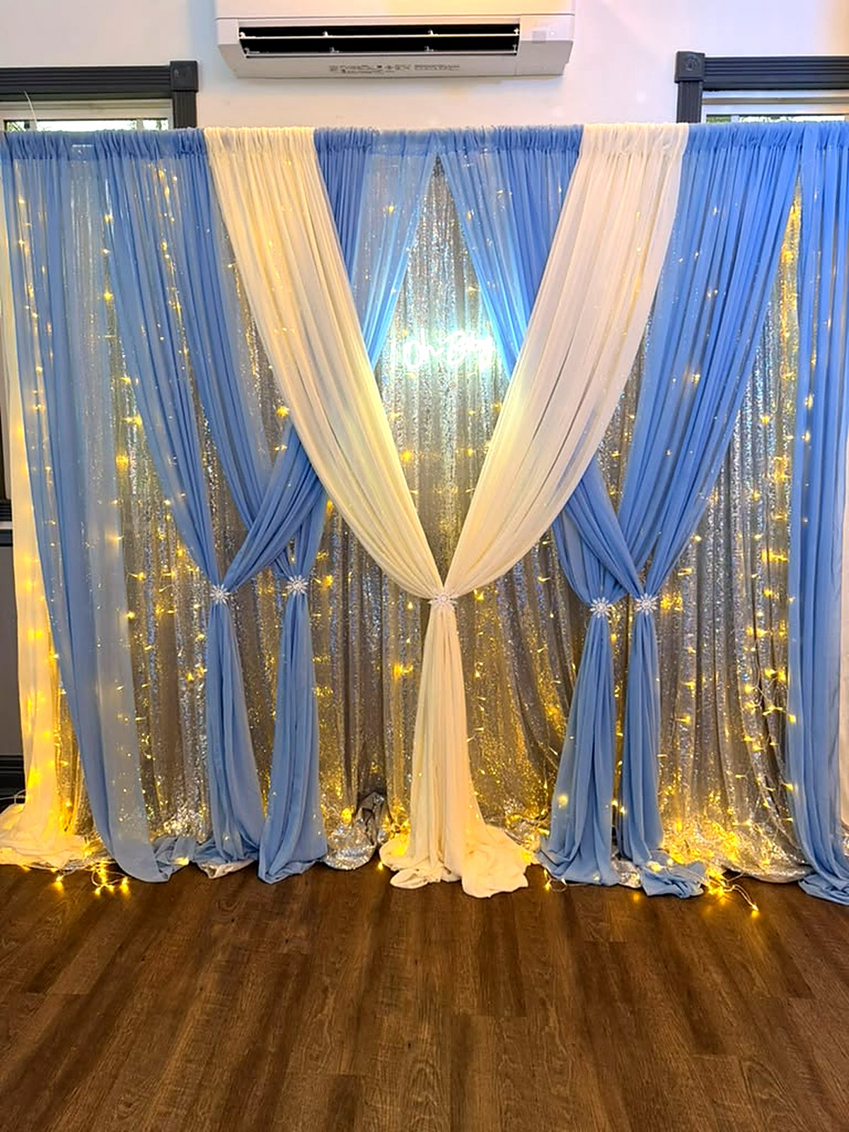 “Oh Baby” neon on a blue and ivory draped sequin backdrop with fairy lights