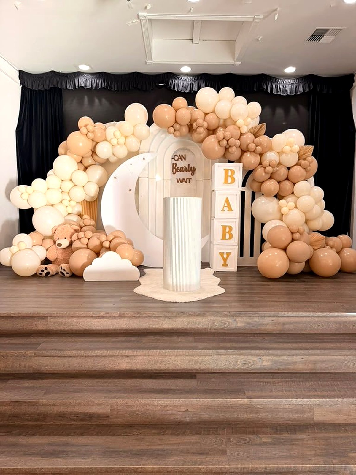 Neutral "Can Bearly Wait" baby shower stage – cream and latte balloon garland, white moon arch, teddy bear and BABY blocks