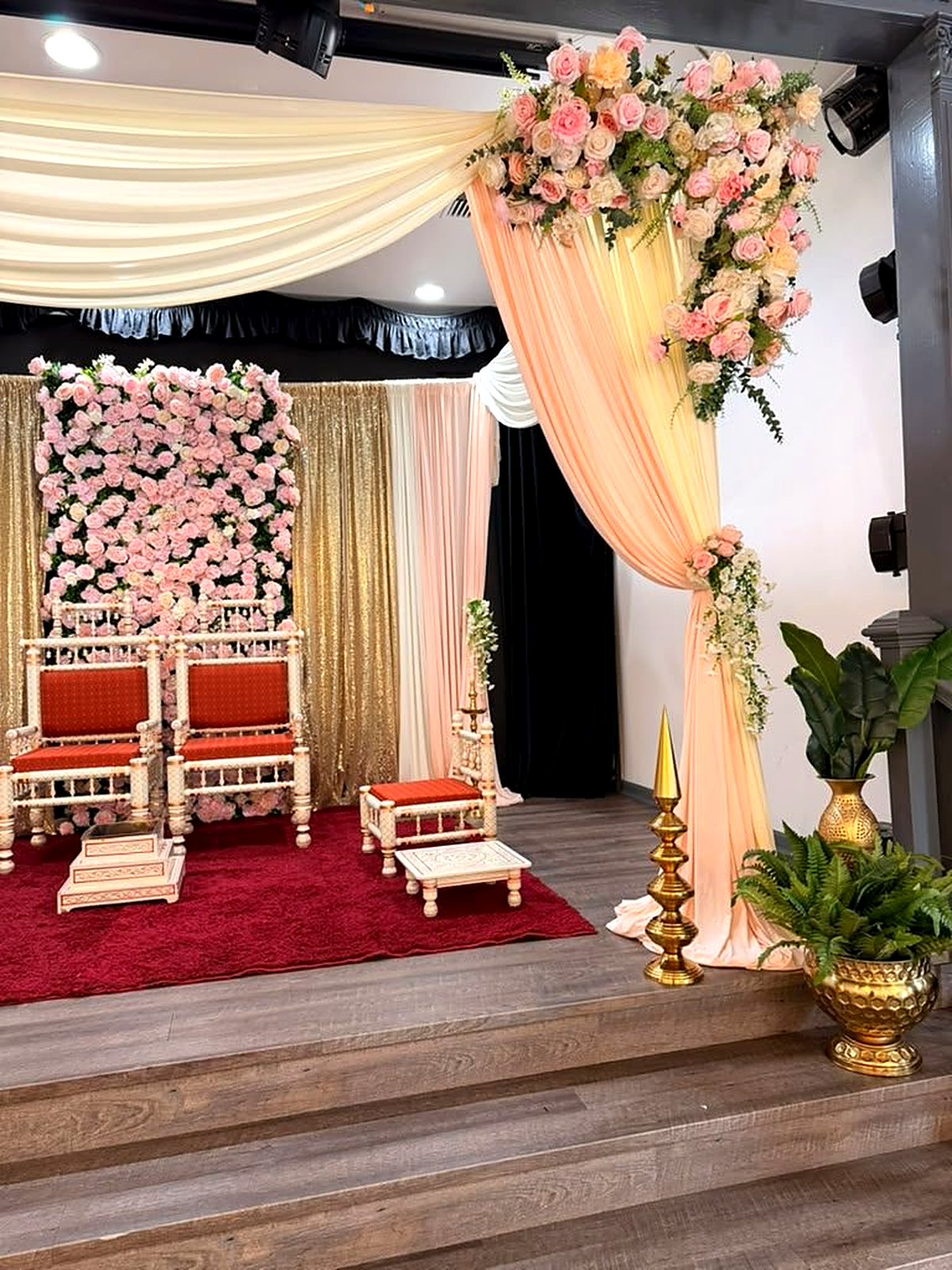 Close-up of the mandap – peach drapes with pink rose cascades, gold sequin panel, carved ivory seating and brass planters