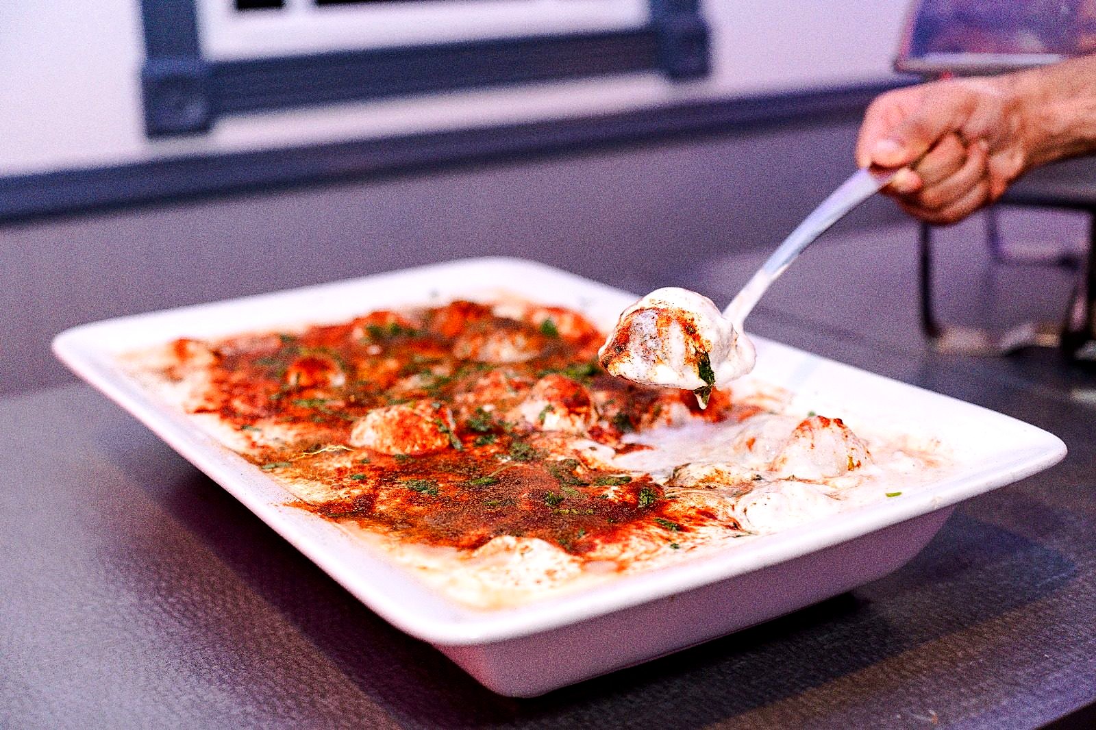Dahi vada in a white serving dish, topped with chili powder and cilantro